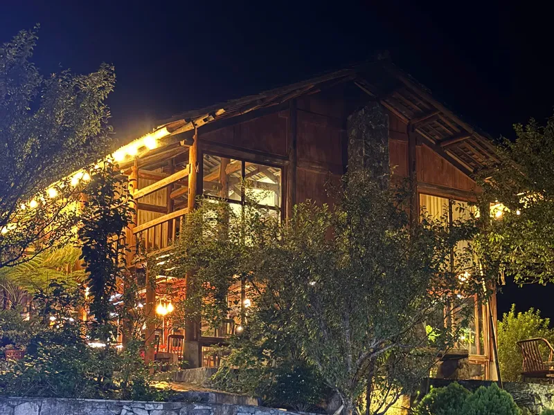 Pa Chi Dua Homestay in Du Gia lit up at night, a wooden lodge above stone garden terraces