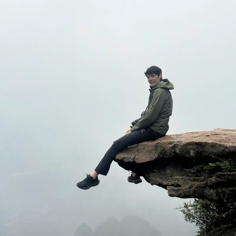 A traveller sitting on a rock ledge above the Nho Que gorge with fog filling the valley below