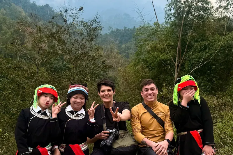 Travellers sitting on a roadside barrier with three young Dao women in embroidered dress