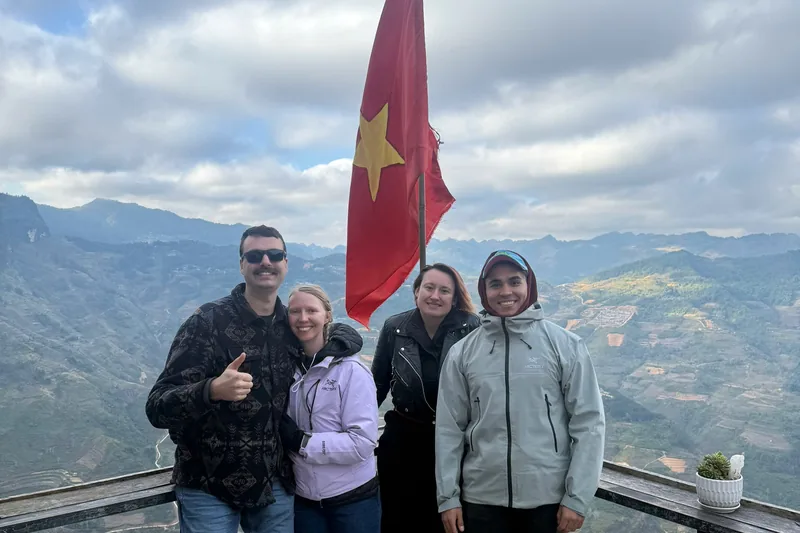 Matt and four travellers at the Vietnamese flag on a viewpoint, terraced mountains behind them