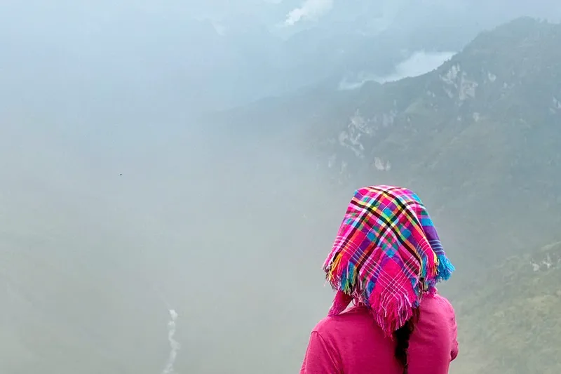 A traveller in a flowered headscarf looking out over a fog-filled canyon, mountains fading into the mist