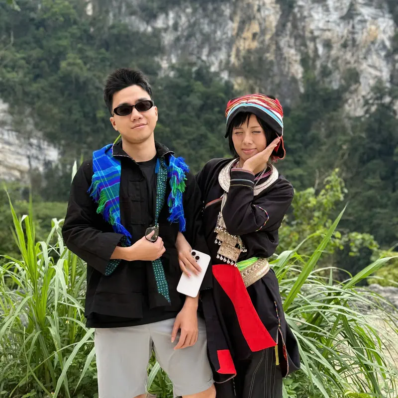 Two people in traditional Hmong dress in front of a limestone cliff