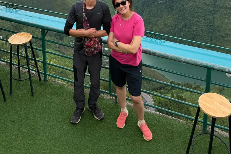 Two travellers at a railed viewpoint above the Nho Que river, karst mountains behind them