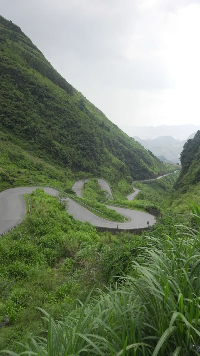 An aerial view of a tight switchback road winding down a green Ha Giang valley