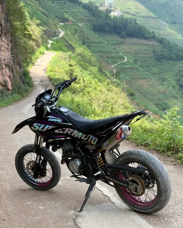 A rider on a dirt bike pointing out across a mountain switchback road toward a winding river valley
