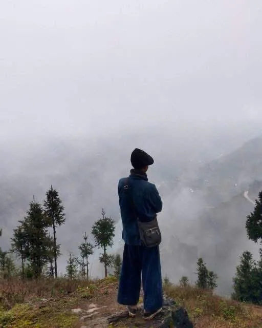 Matt looking out over a mist-filled valley in Ha Giang, back to camera, in a traditional indigo jacket